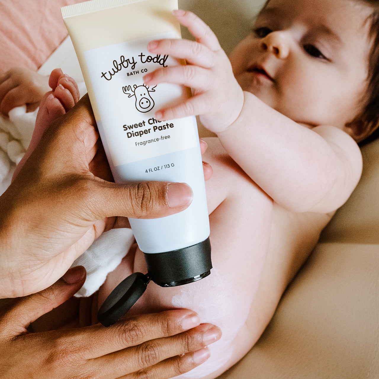 Mom rubbing her baby's bum using Diaper Paste on the bed.